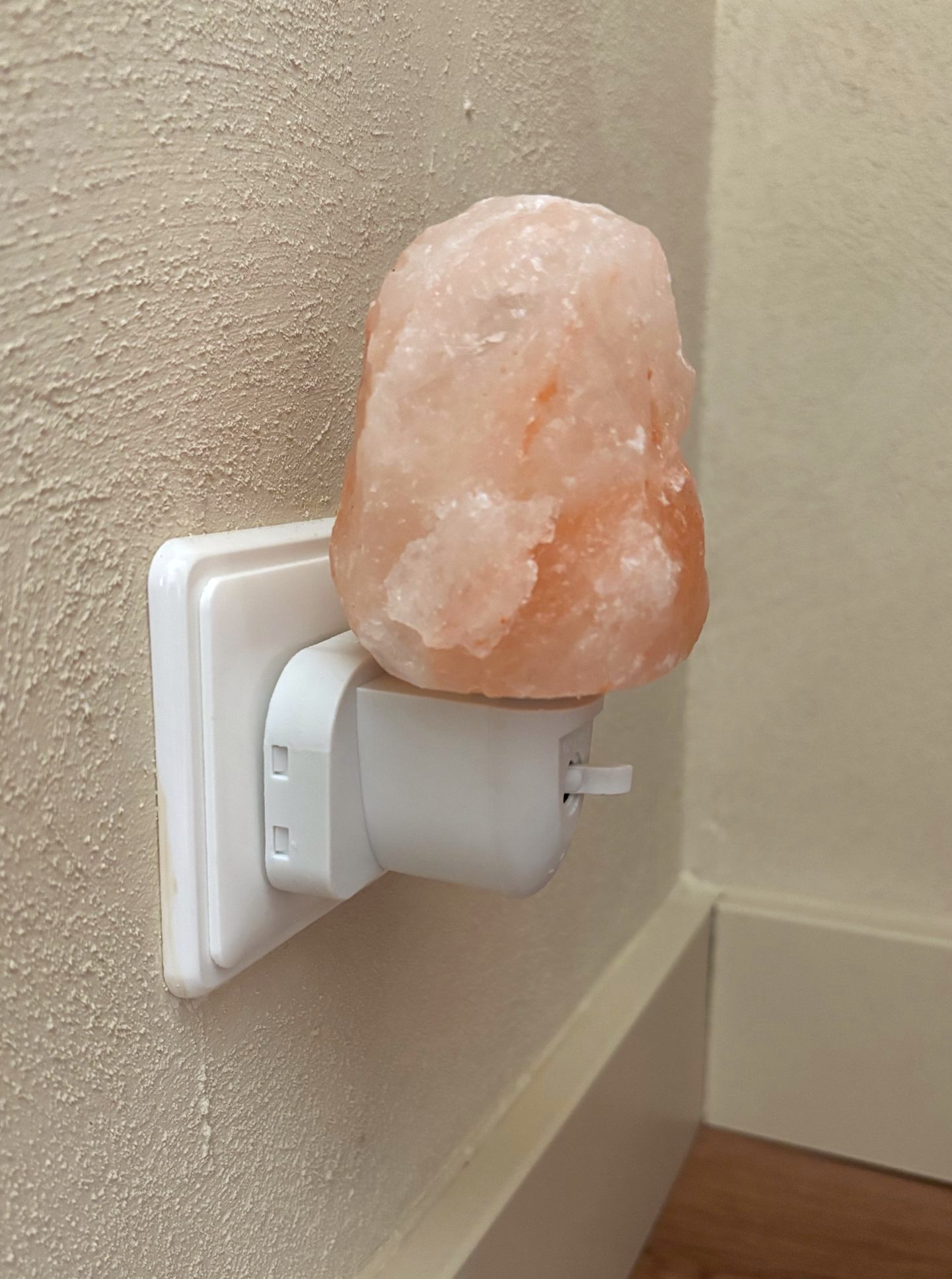Een roze zoutlamp, aangesloten op een stopcontact in een hoek.
