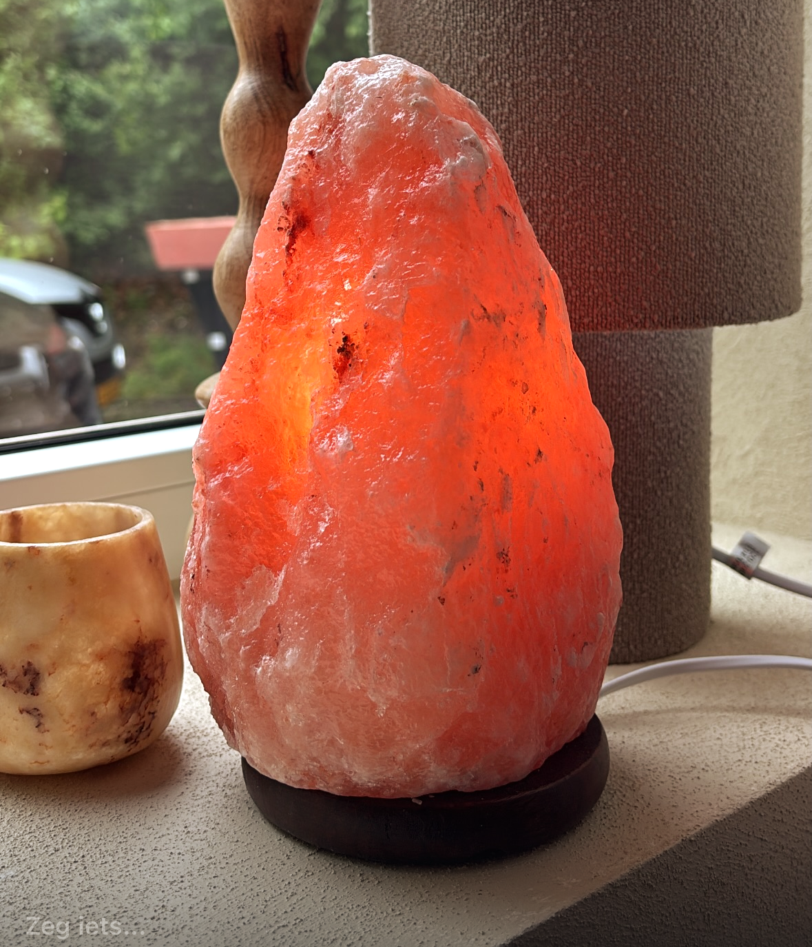 Een feloranje Himalaya-zoutlamp op een zwarte voet bij een raam.