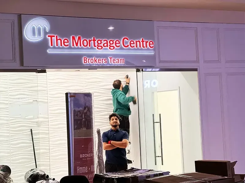 Two people standing at the entrance of The Mortgage Centre storefront, one holding a ladder inside.