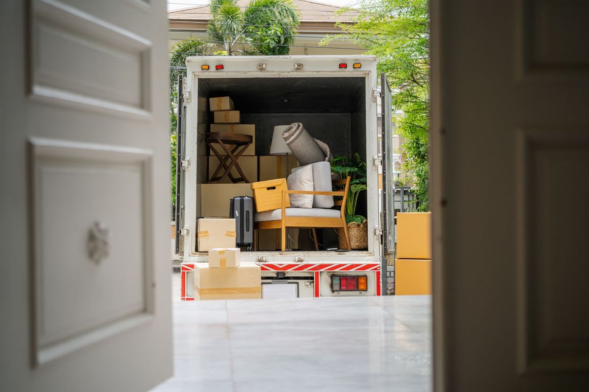 Moving truck loaded with boxes and furniture, seen through a doorway in a driveway.