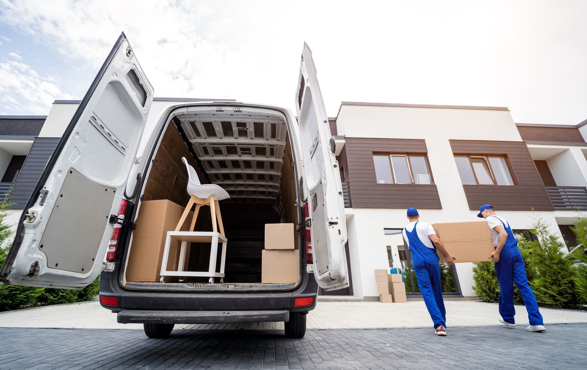 Moving truck with open rear doors being unloaded outside a modern house by two workers