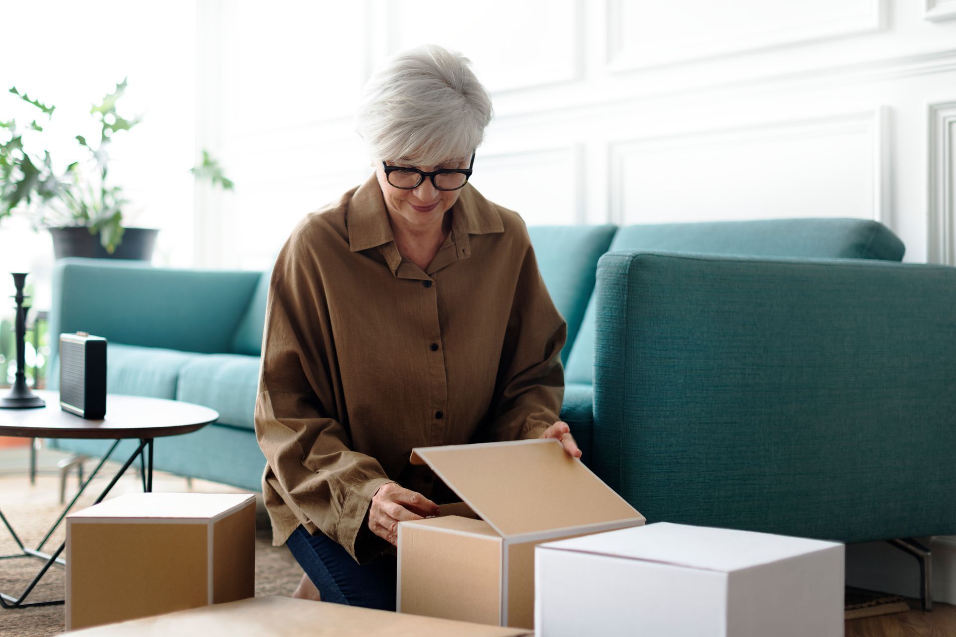 Person unpacking cardboard boxes in a bright living room with a teal sofa