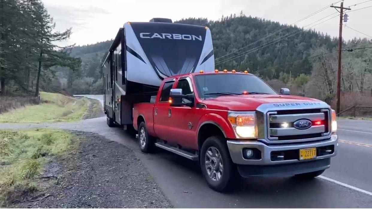 Red pickup truck towing a large white and black RV on a road in a rural area.