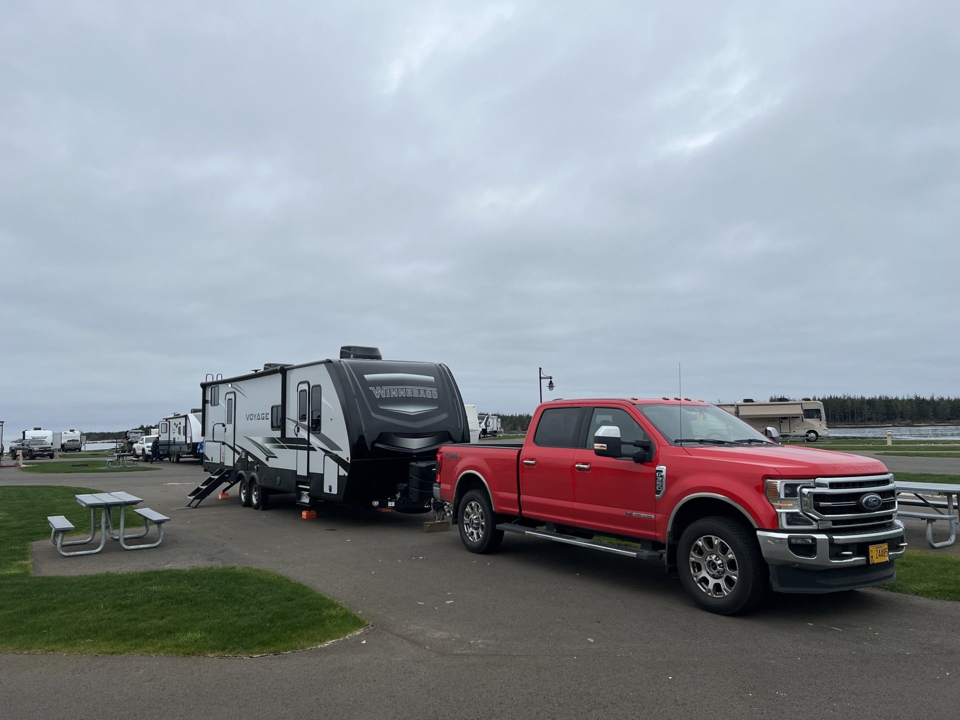 Red pickup truck towing a black and white travel trailer at a campground on an overcast day.