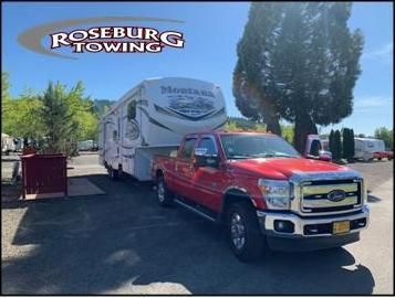 Red truck towing a Montana RV, Roseburg Towing logo in top left, sunny outdoor setting.