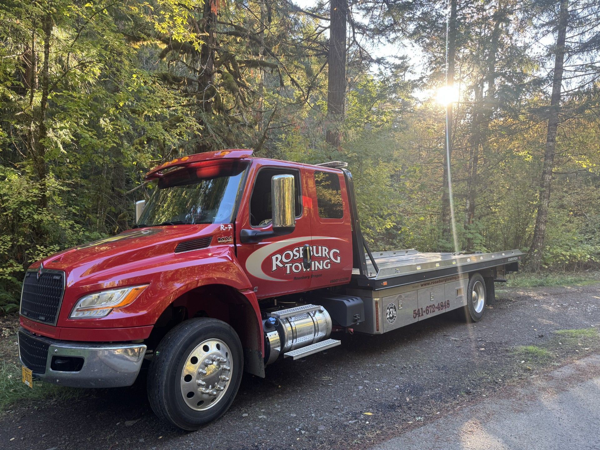 Red tow truck parked on a gravel road, forest background, sunny.