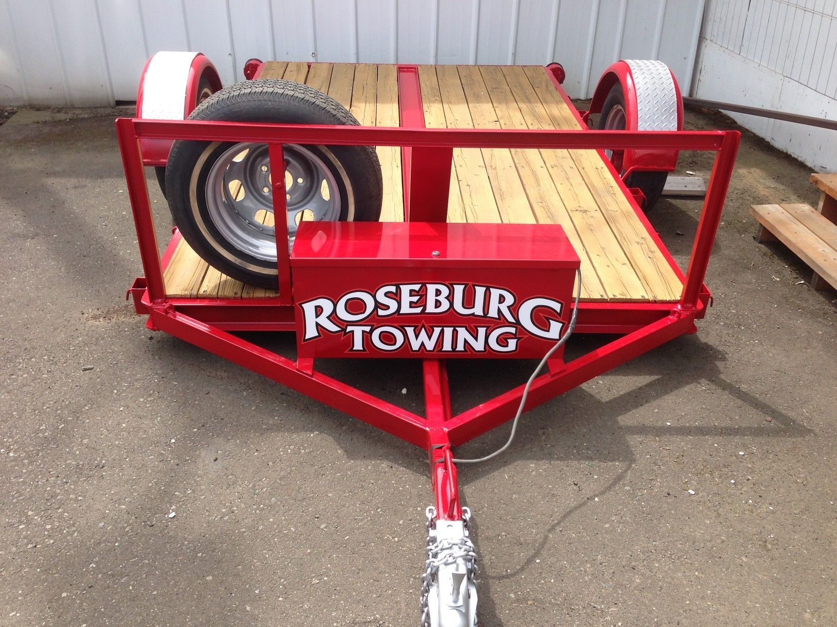 Red Roseburg Towing trailer on concrete, wooden bed, spare tire, white wheels.