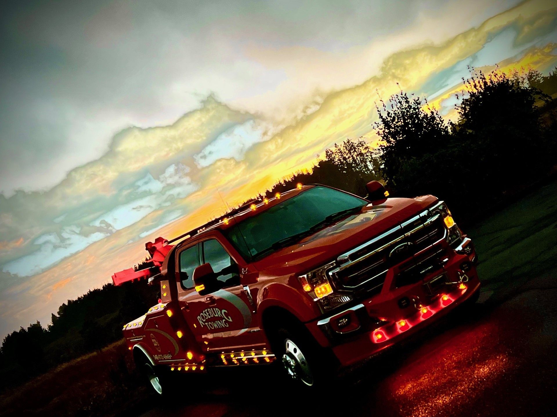 Red tow truck with flashing lights against a sunset sky.