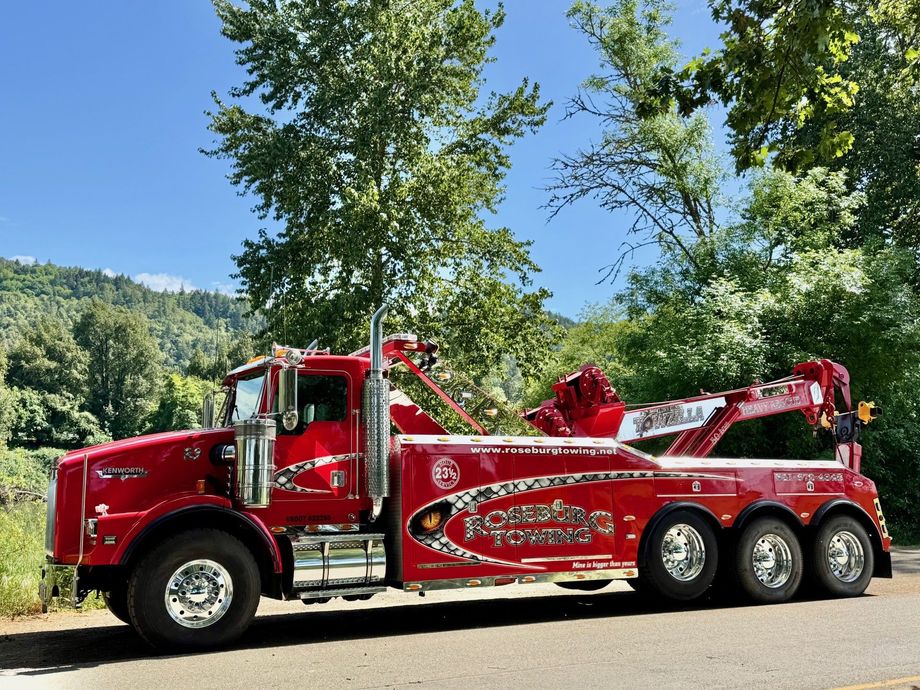Red tow truck parked on the side of a road, with trees and a hillside in the background.