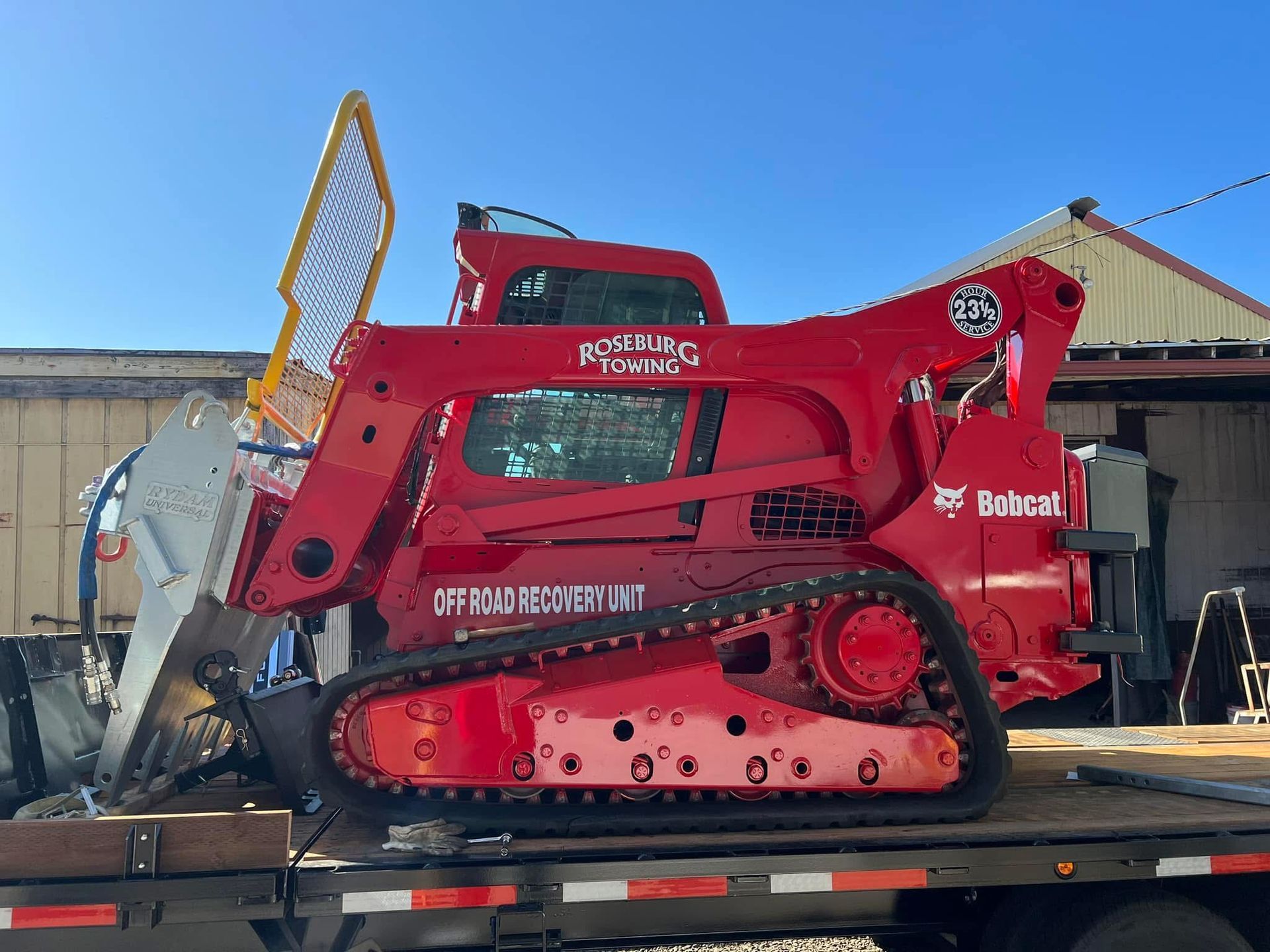 Red Bobcat compact track loader with attached forestry cutter on a flatbed trailer.