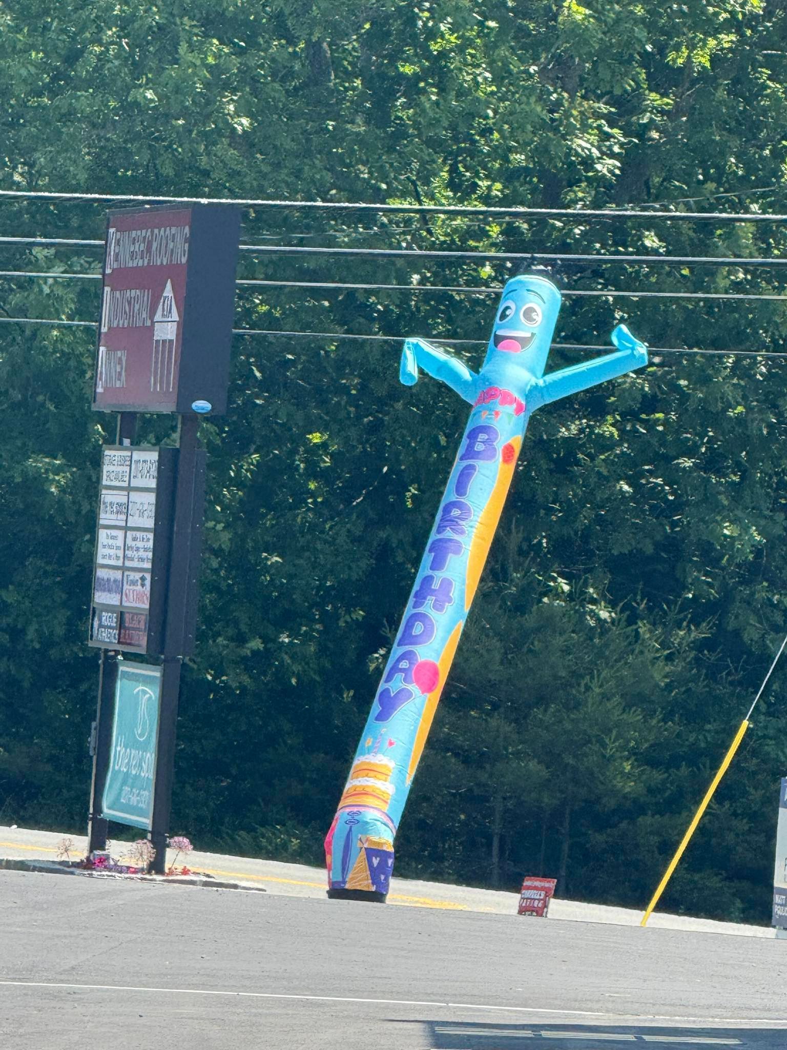 A blue and yellow air dancer with a sign in the background that says ' coca cola '