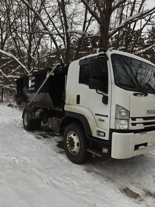 White Isuzu dump truck parked on snow-covered ground near bare trees.