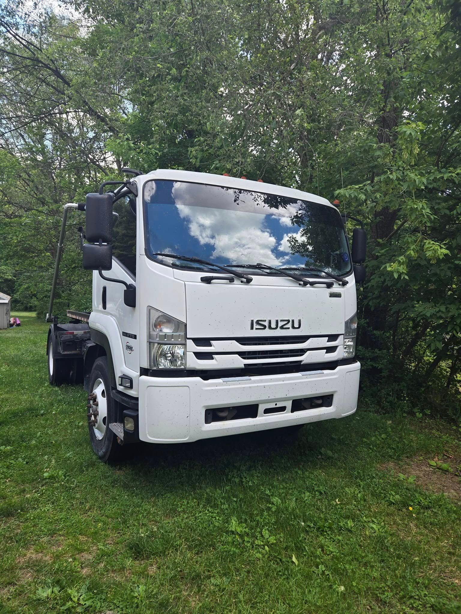 A white truck is parked in the grass in front of trees.