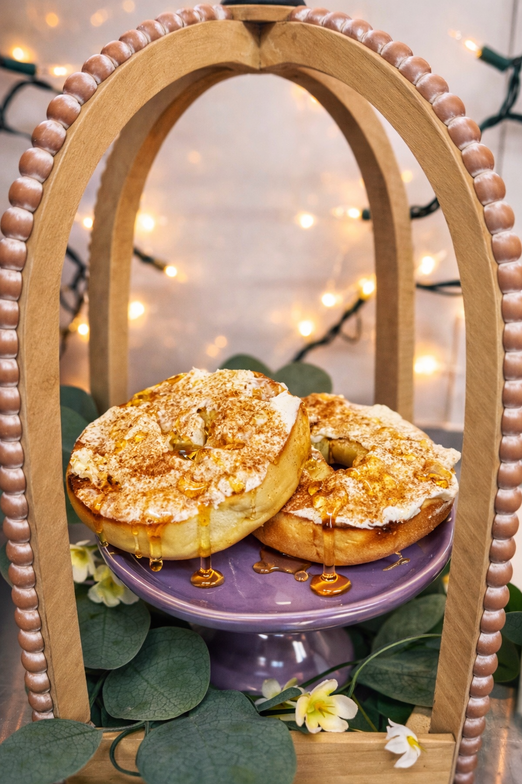 Two bagels with cream cheese and honey on a purple stand within a wooden arch.