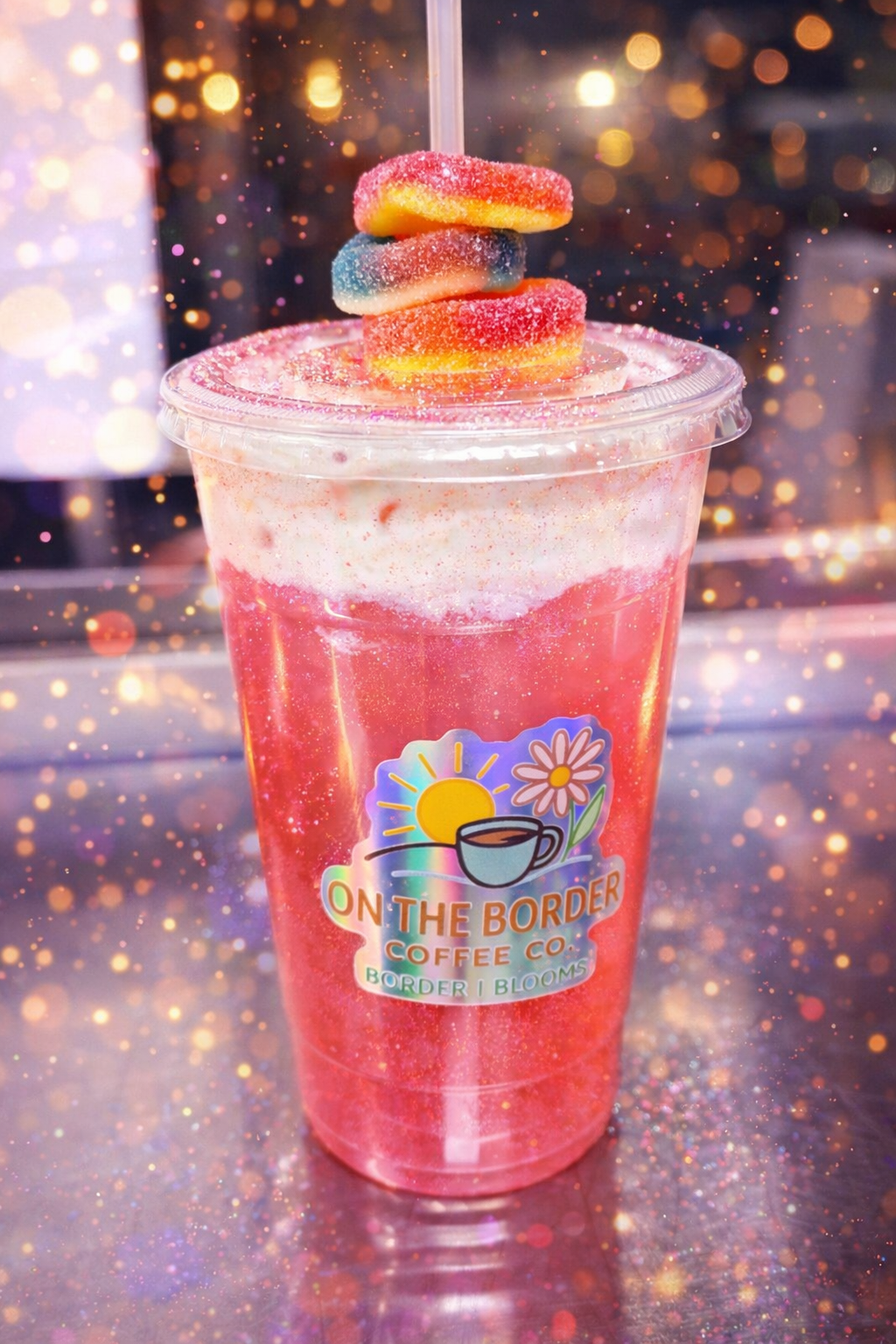 Pink layered drink in clear cup with gummy candies on top, 