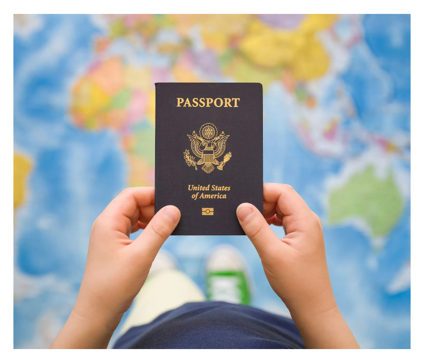 Niño sosteniendo un pasaporte estadounidense frente a un mapa del mundo borroso.