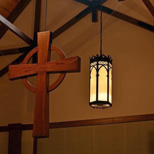A central cross hanging from the interior of St. James Episcopal Church with beams and a chandelier in view