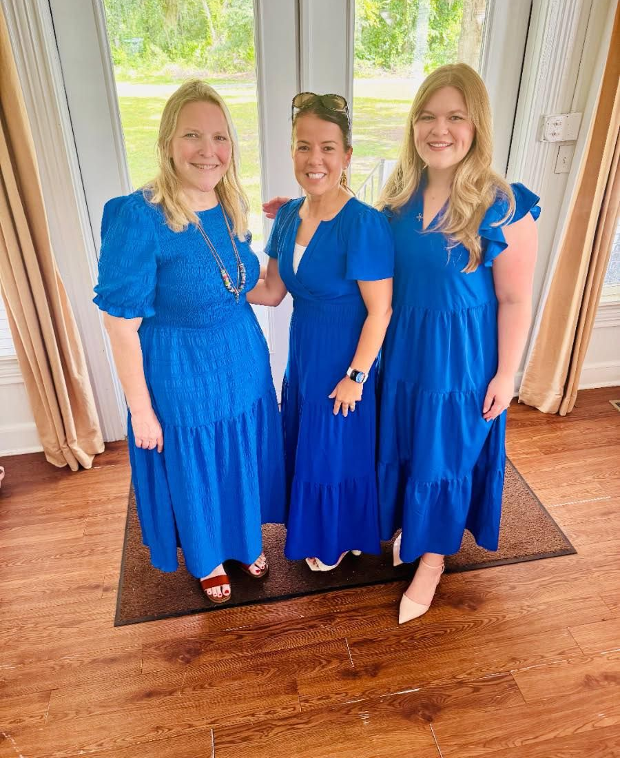 Three women of Daughters of the King stand in their blue dresses in front of double glass doors at Parish Hall