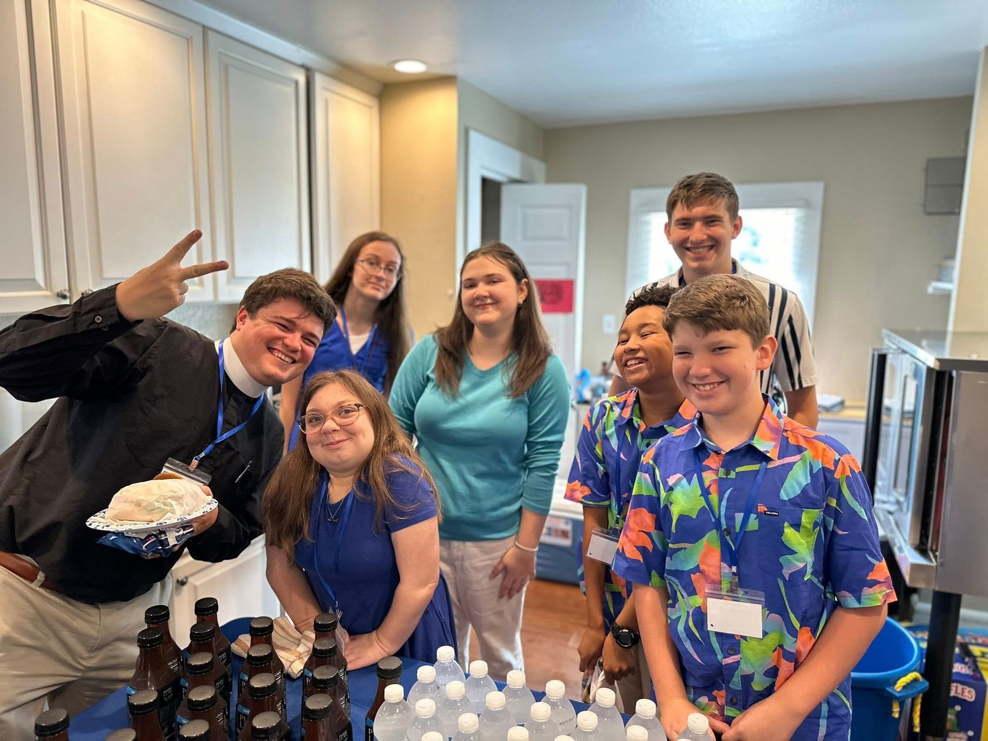 Fr. William with a group of youth and bottled water in front of them in the kitchen