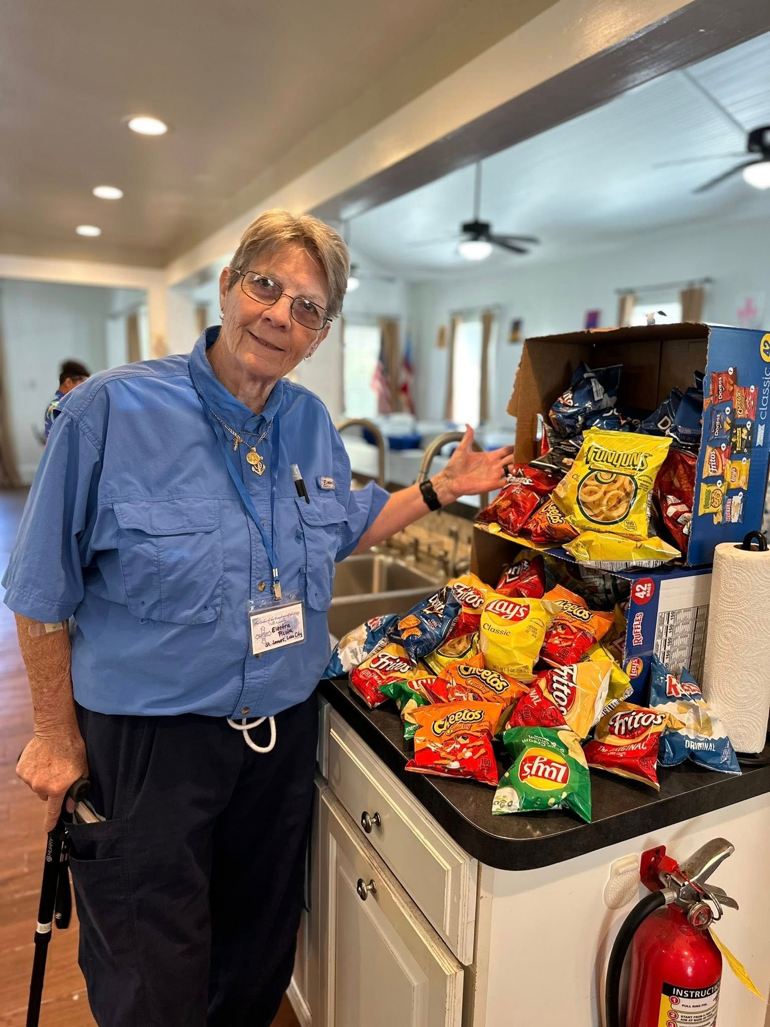 A Feed My Lambs volunteer stands in front of a large assortment of chips to be given out