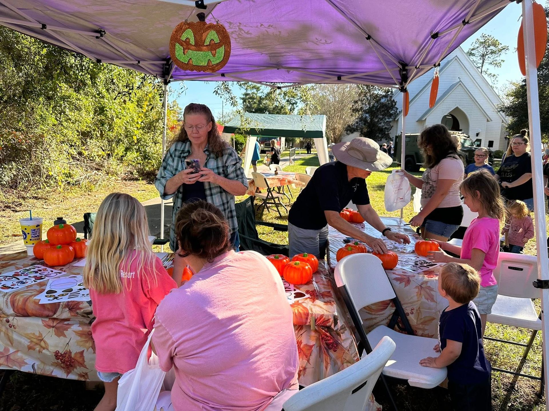 Children, parents, and volunteers gather under a tent to decorate pumpkins during Family Fall Festival