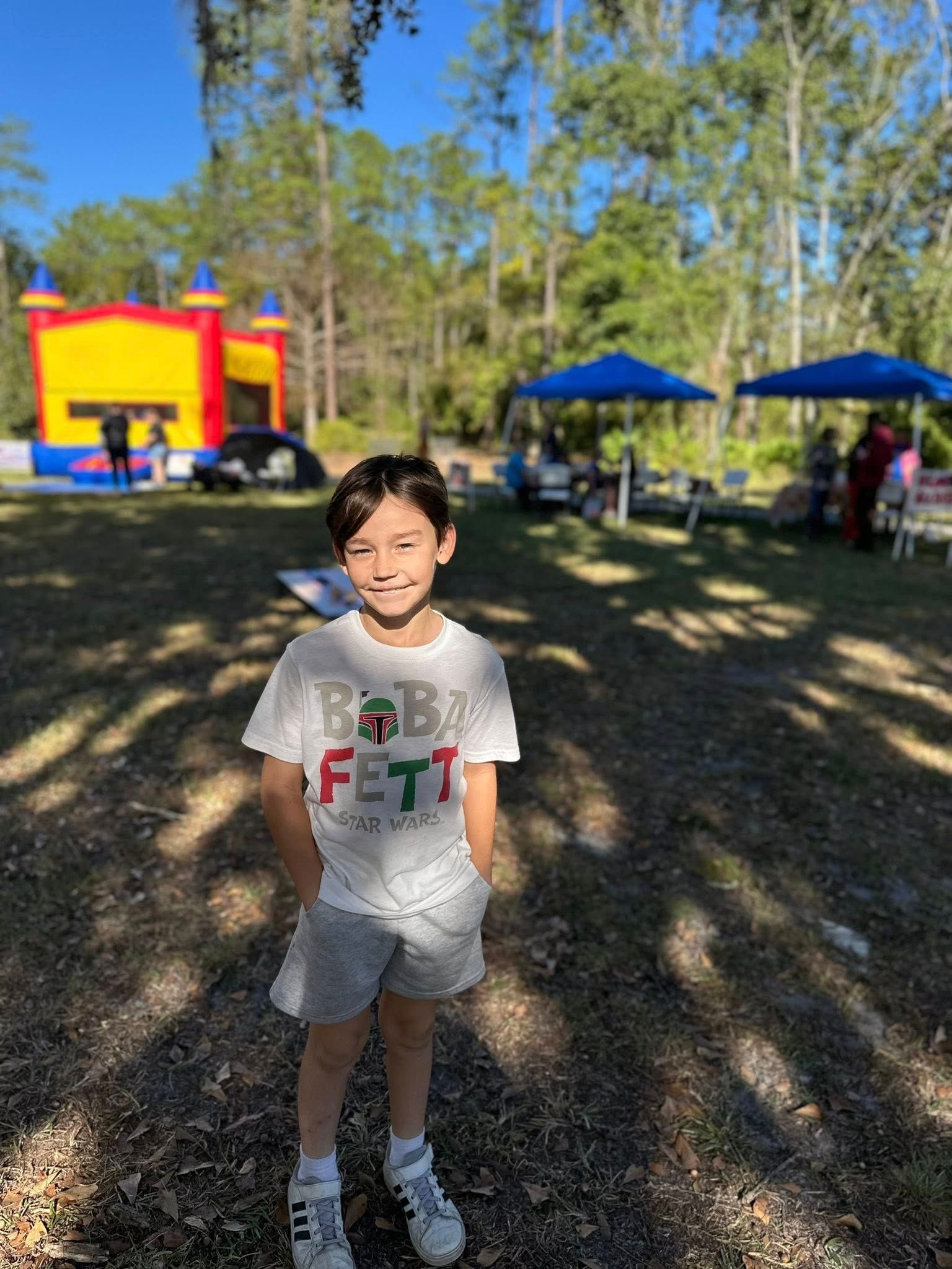 A child stands in front of tents and a bouncy house on church grounds during Family Fall Festival