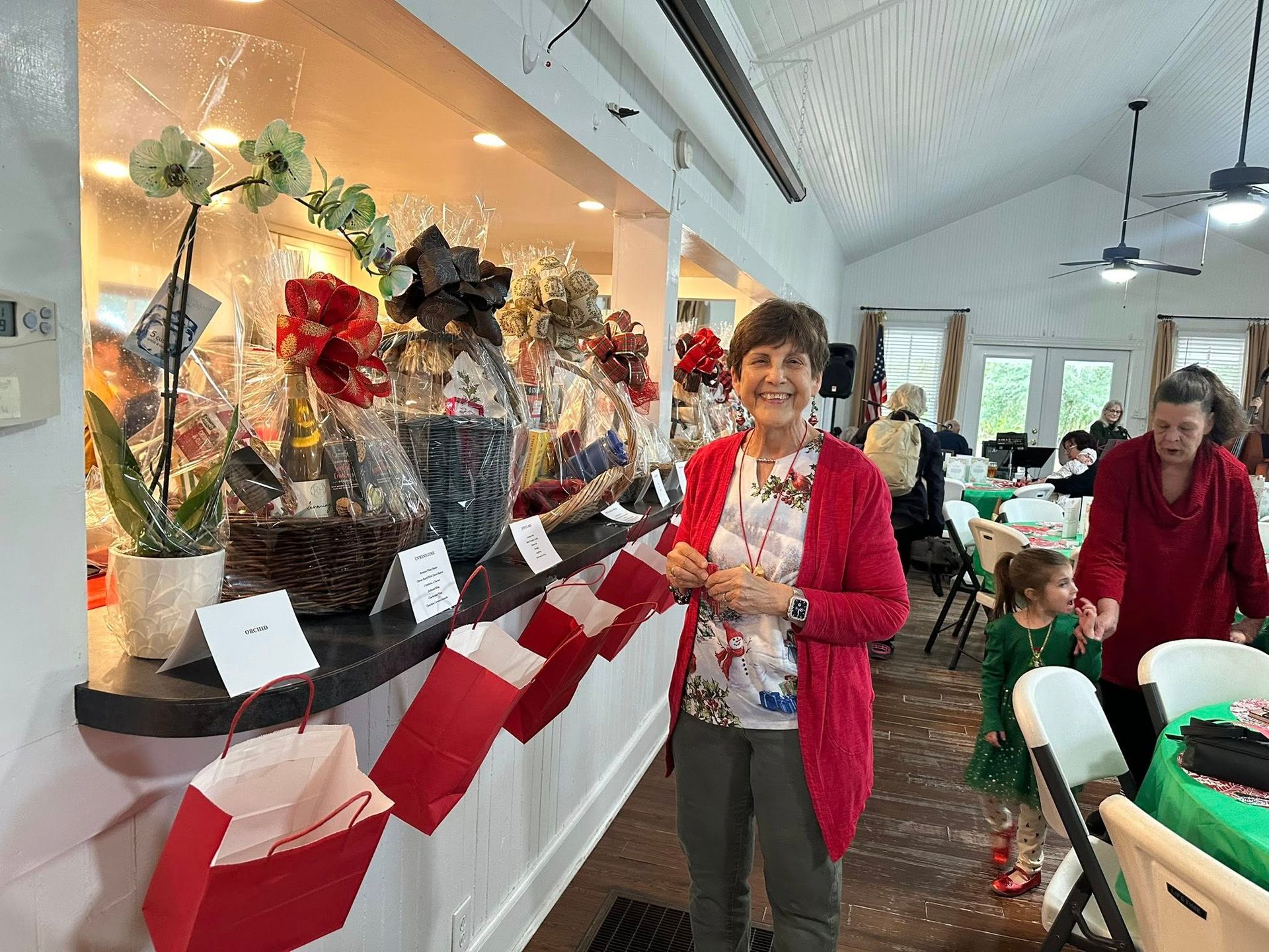A row of flowery baskets all in a row with red bangs hung underneath them and a smiling churchgoer in red
