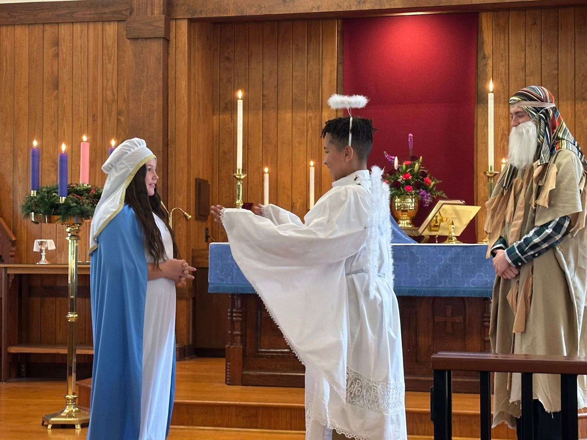 A boy dressed as an angel in white animatedly speaks to a girl dressed in a blue Mary costume