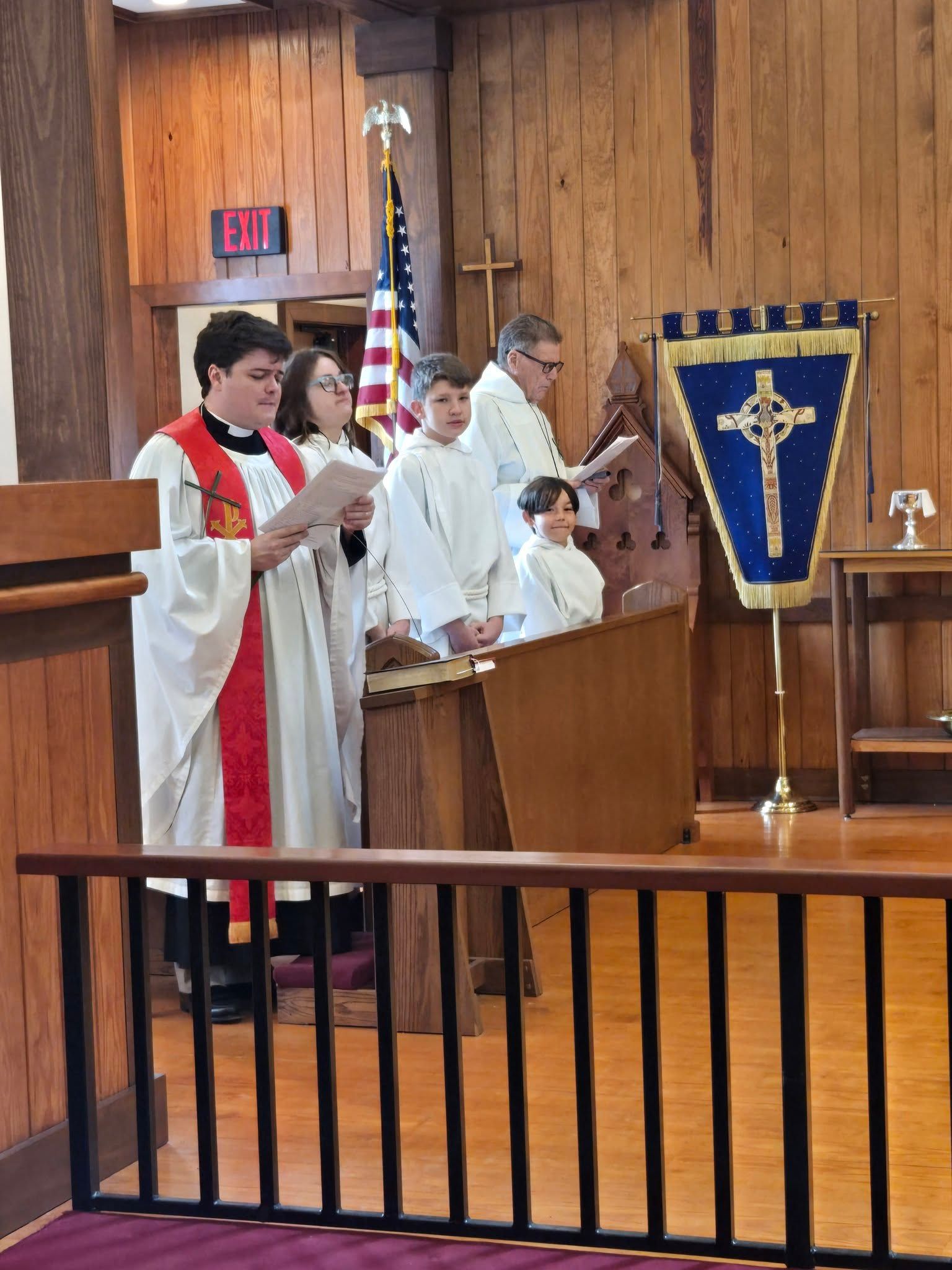Fr. William stands reading from a service bulletin alongside other church worship assistants dressed in their white vestments