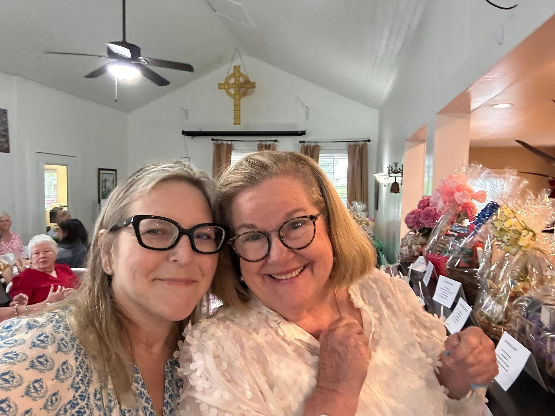 Two women smile in front of some decorated baskets with a cross in the background.