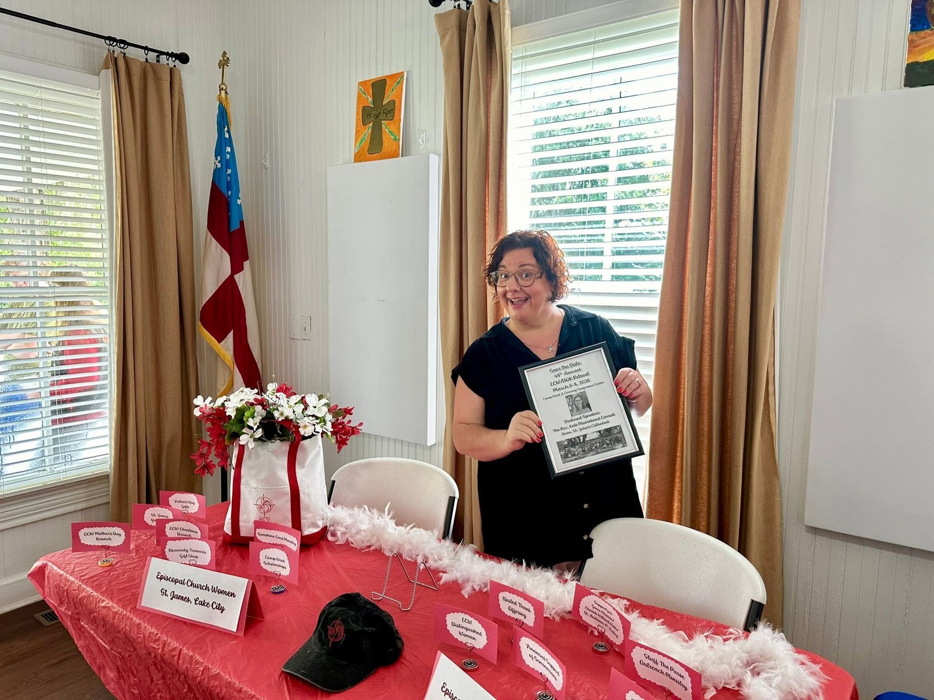 A woman stands in front of a red decorated table with information about ECW in her hands.
