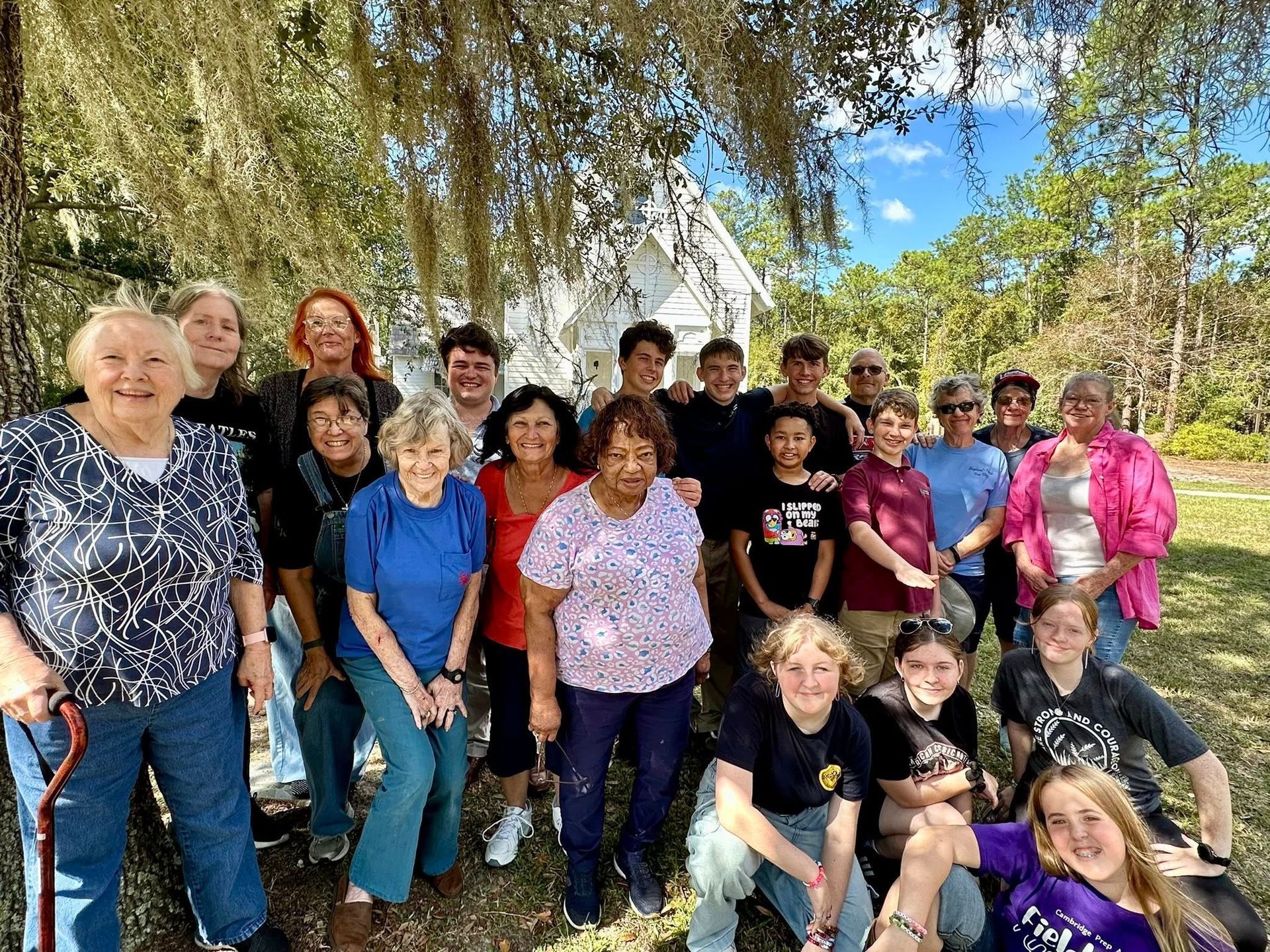 A large group of church members standing under a tree with the Historic Chapel of St. James behind them