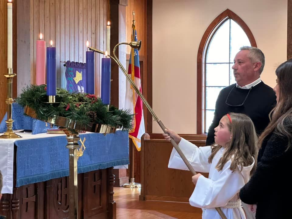 A child acolyte lights the advent candle with other members standing behind