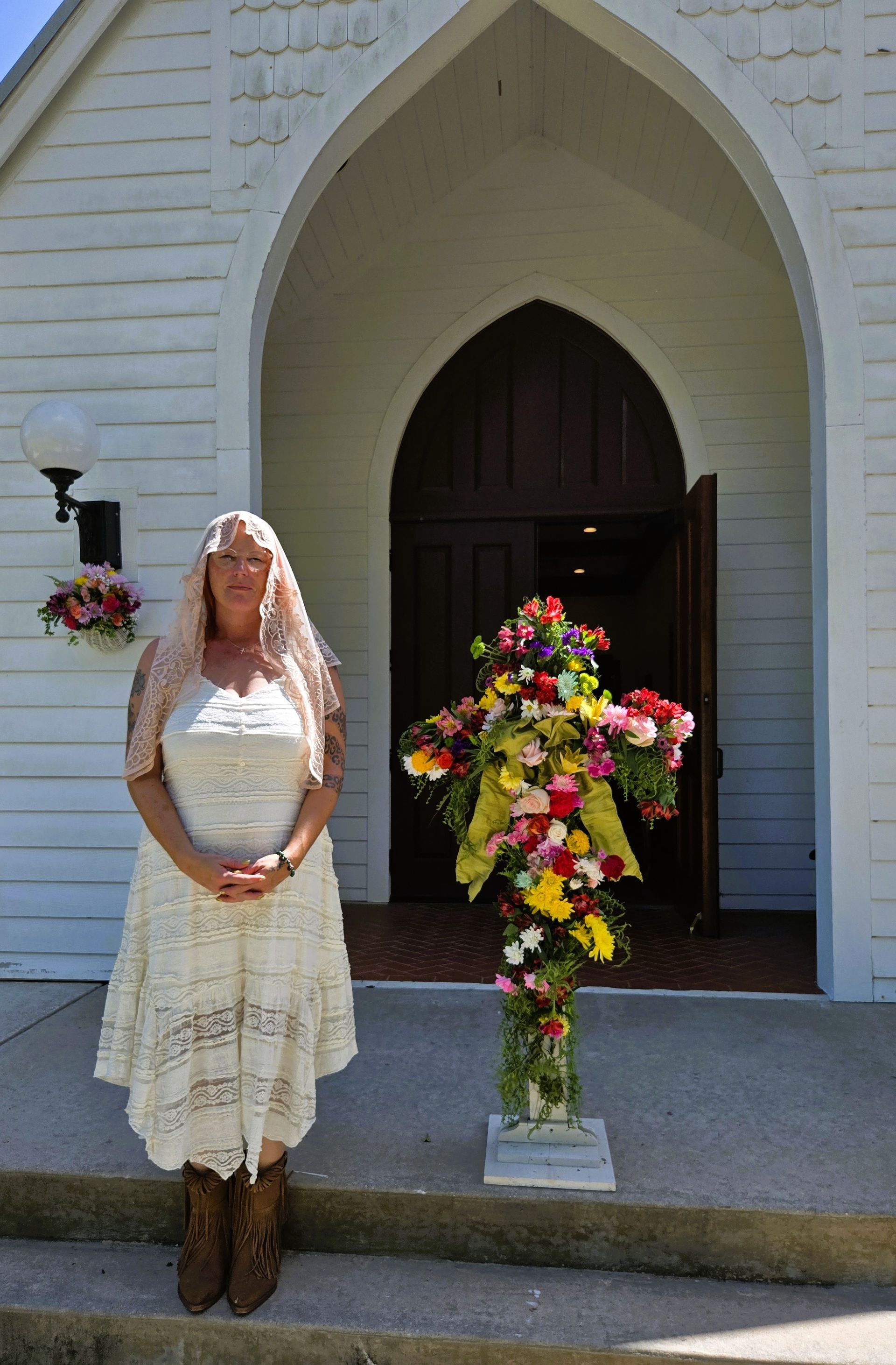 A staff member in a white veil and white dress standing in front of St. James Episcopal Church door 