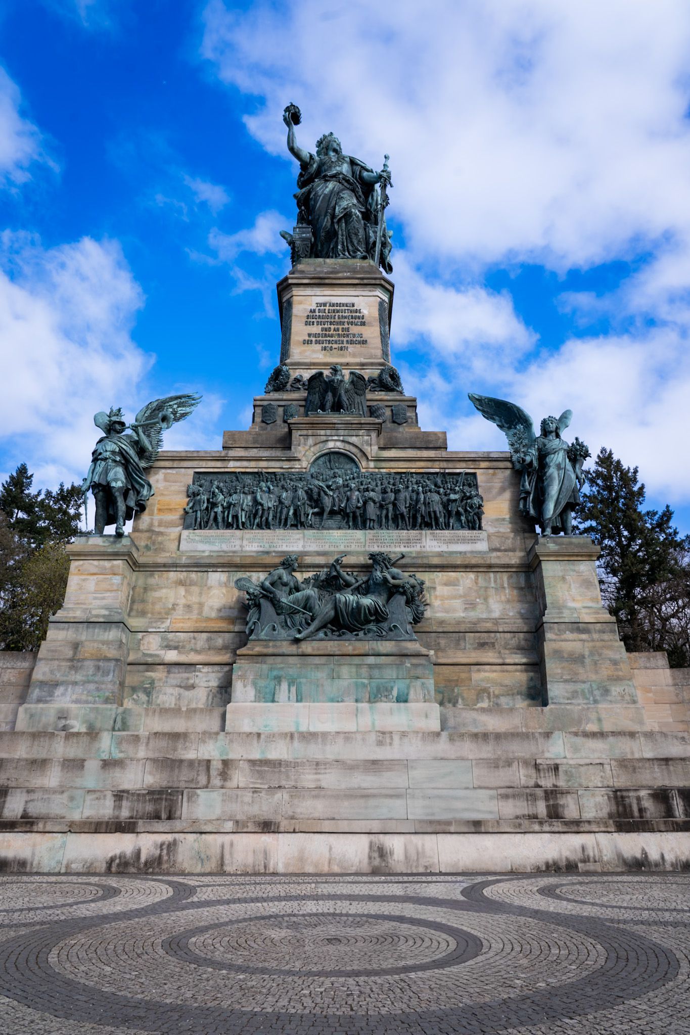 Large bronze monument on stone steps beneath a bright blue, cloudy sky