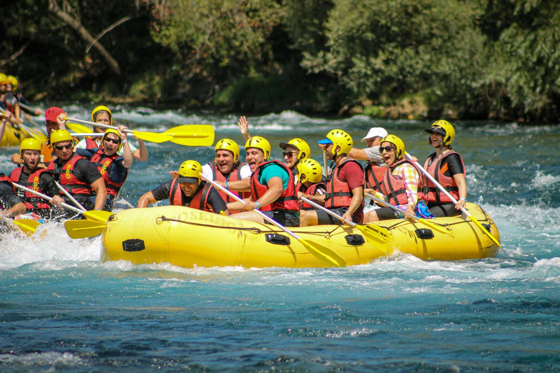 Group rafting in a bright yellow inflatable raft on a fast-moving river, with green trees in the background