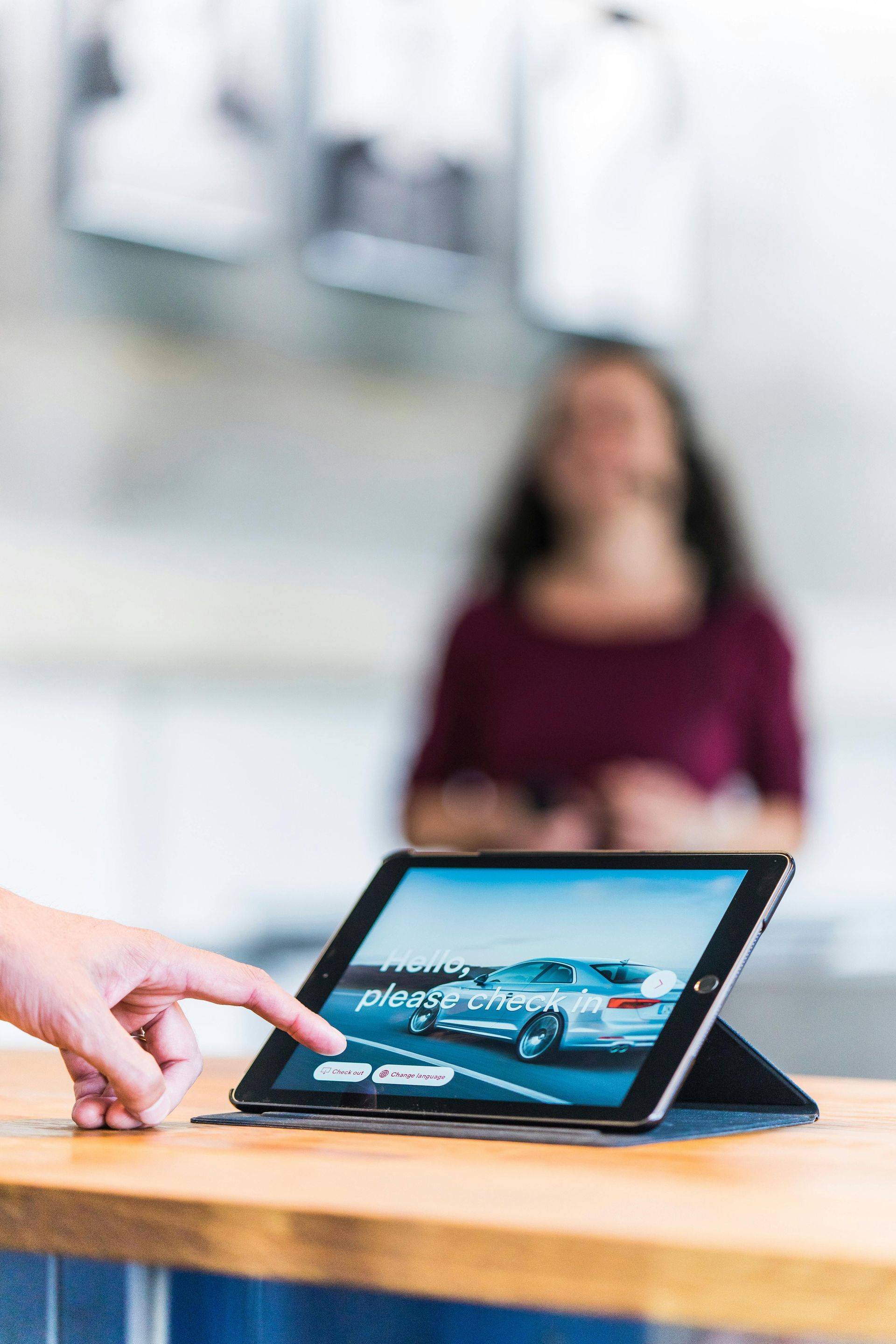 Hand pointing at a tablet on a wooden table showing a blue car in a showroom