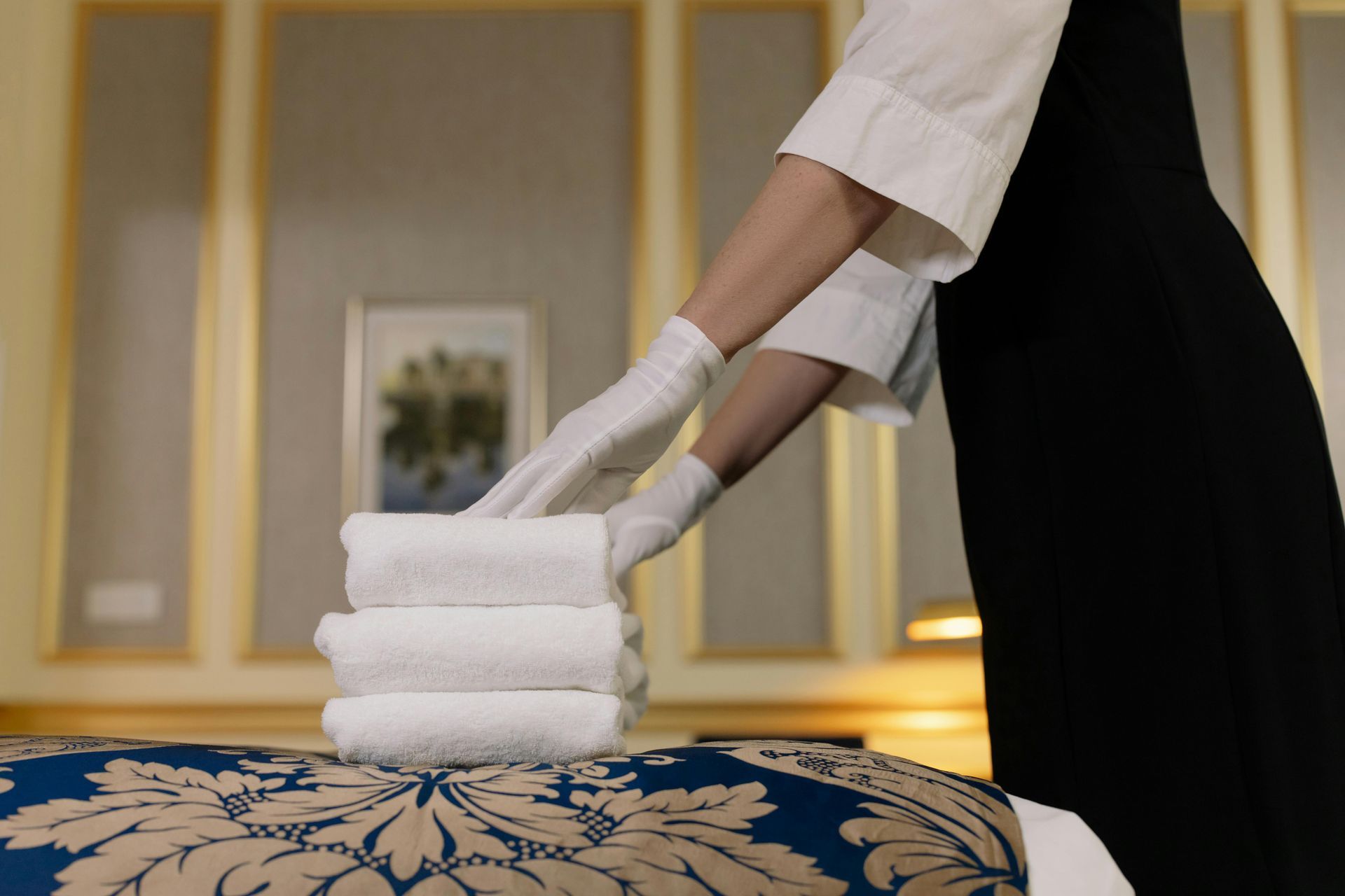 Spa worker stacking white towels on a massage table with a blue patterned cover