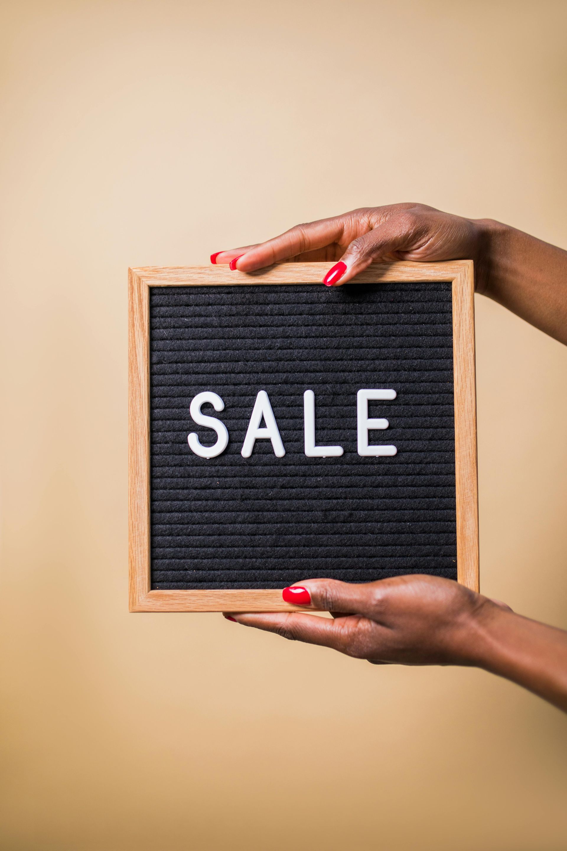 Hands holding a small black board with the word “SALE” on a beige background