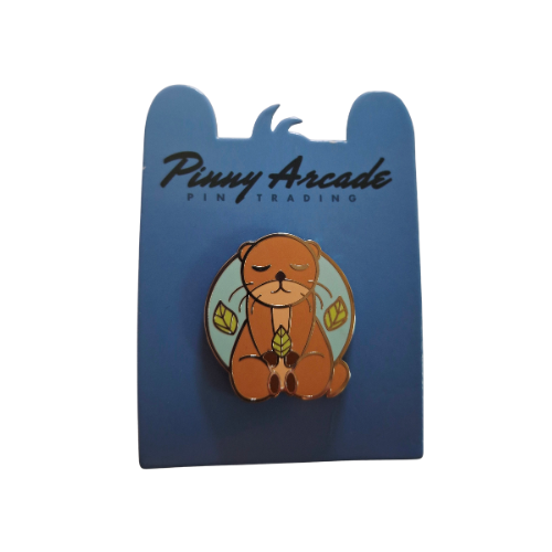 Otter pin on blue card. Brown otter with closed eyes, holding leaves.