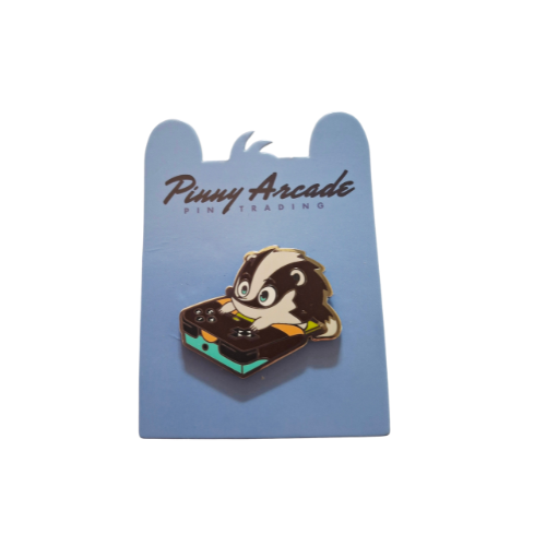Badger enamel pin on blue card. Badger sits on a game console with