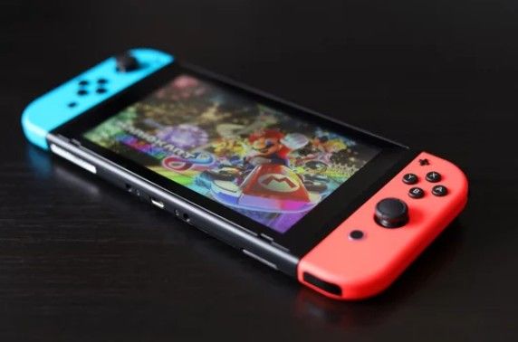 Nintendo Switch with neon blue and red Joy-Cons displaying a colorful game screen on a dark surface