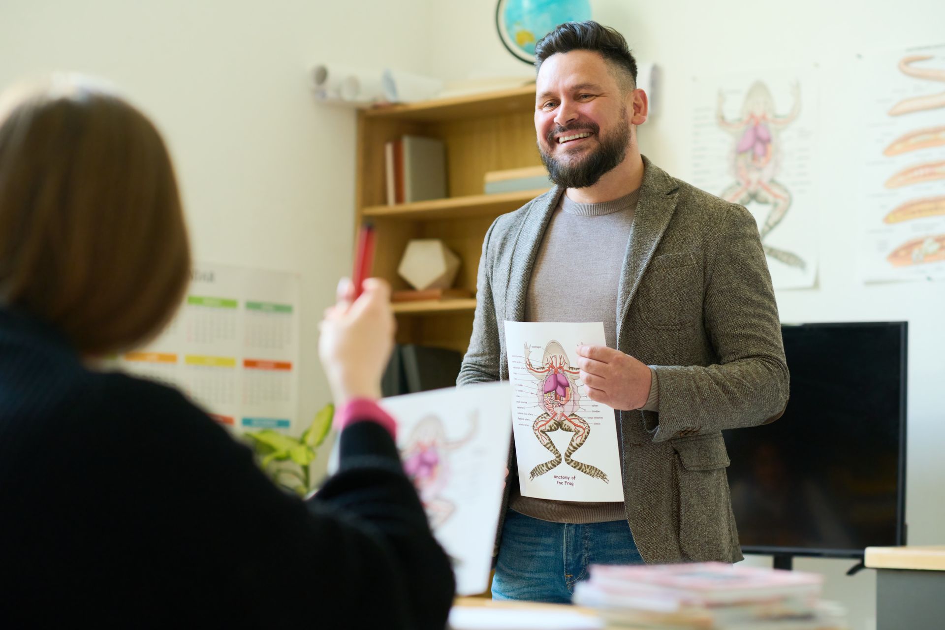A man is holding a picture of a frog in front of a woman in a classroom.