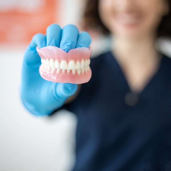 A gloved hand holds up a set of dentures for a dental procedure.