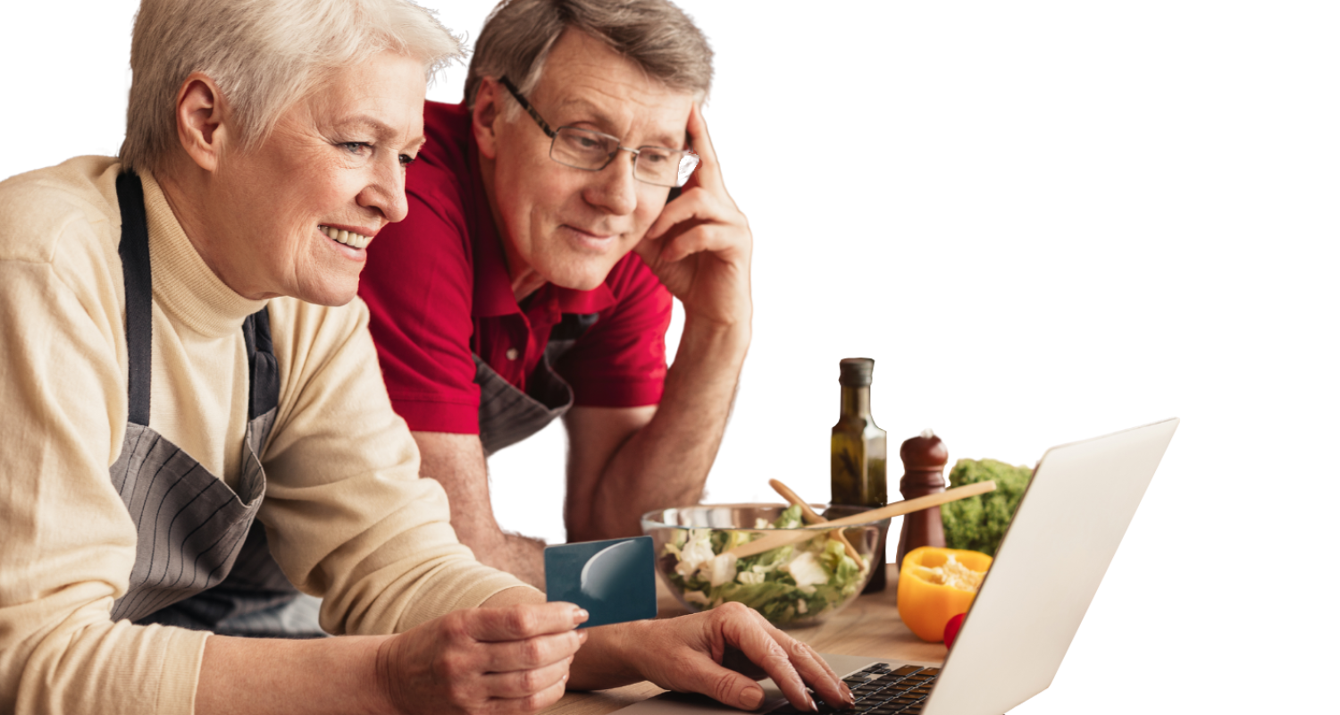 Two people wearing aprons in a kitchen look at a laptop while one holds a credit card near a bowl of salad.
