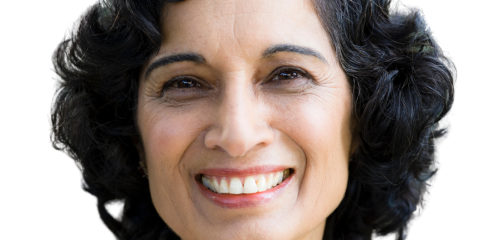 A person with dark, wavy hair smiling warmly at the camera against a white background.