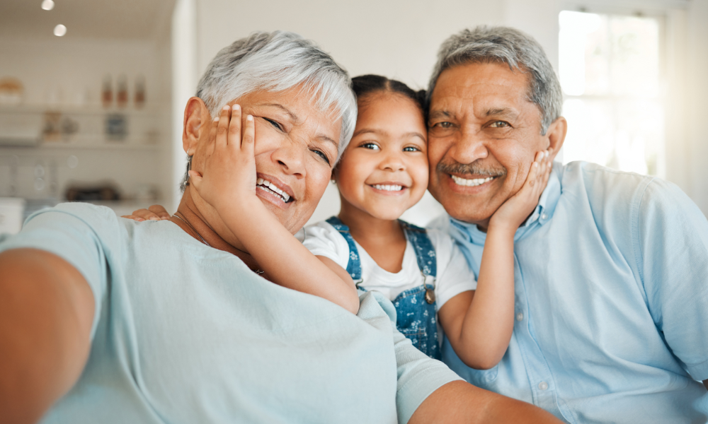 A smiling child poses for a selfie between an older woman and an older man, all three with their hands on their cheeks.