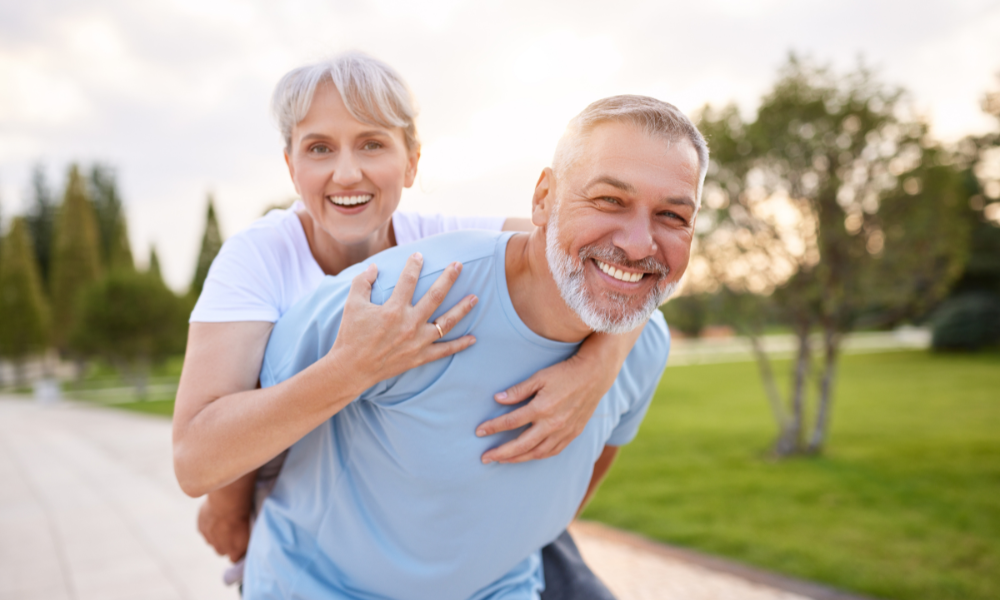 A joyful couple outdoors, with one person giving the other a piggyback ride on a park pathway.