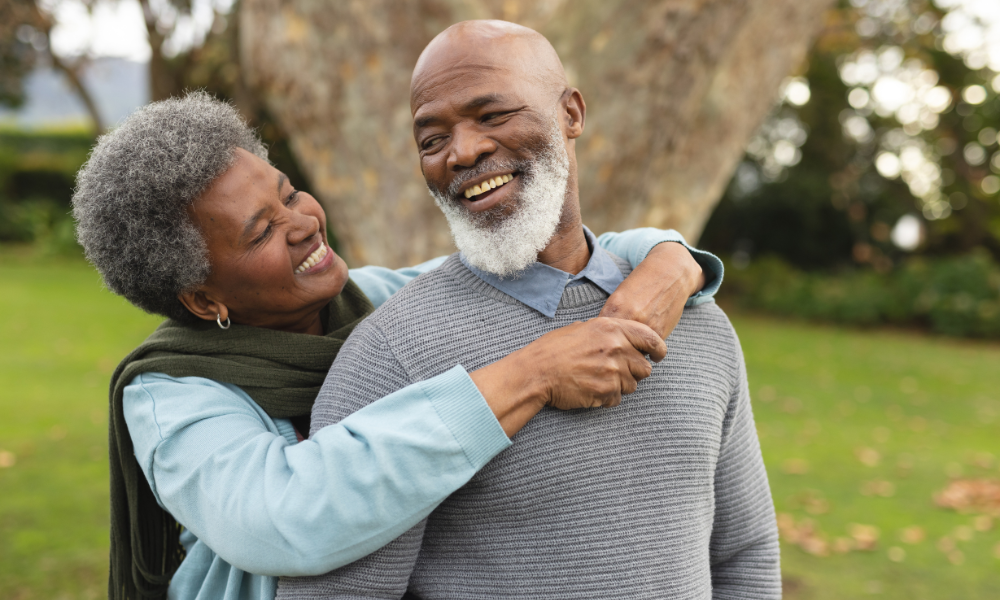 An affectionate couple embraces in a park, smiling at each other.