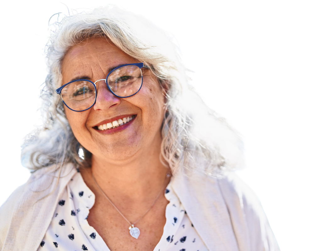 A smiling person with wavy gray hair wearing dark-rimmed glasses and a white patterned shirt with a necklace.
